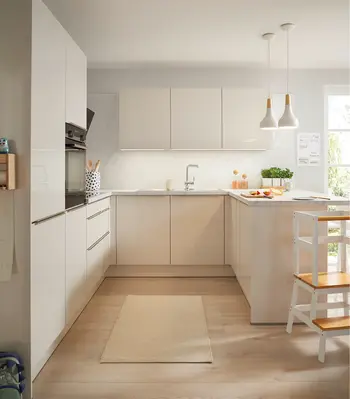 Moderne weiße Küche mit grifflosen Fronten, U förmigem Grundriss, heller Arbeitsplatte und Holzfußboden. Pendelleuchten, integrierte Elektrogeräte und viel Tageslicht schaffen eine freundliche und funktionale Küchenlösung.